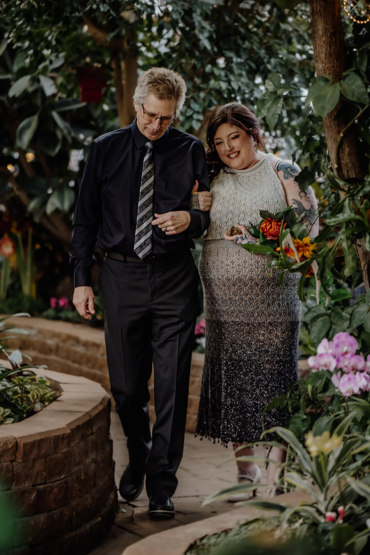 Father walking his daughter down a greenhouse aisle surrounded by tropical foliage