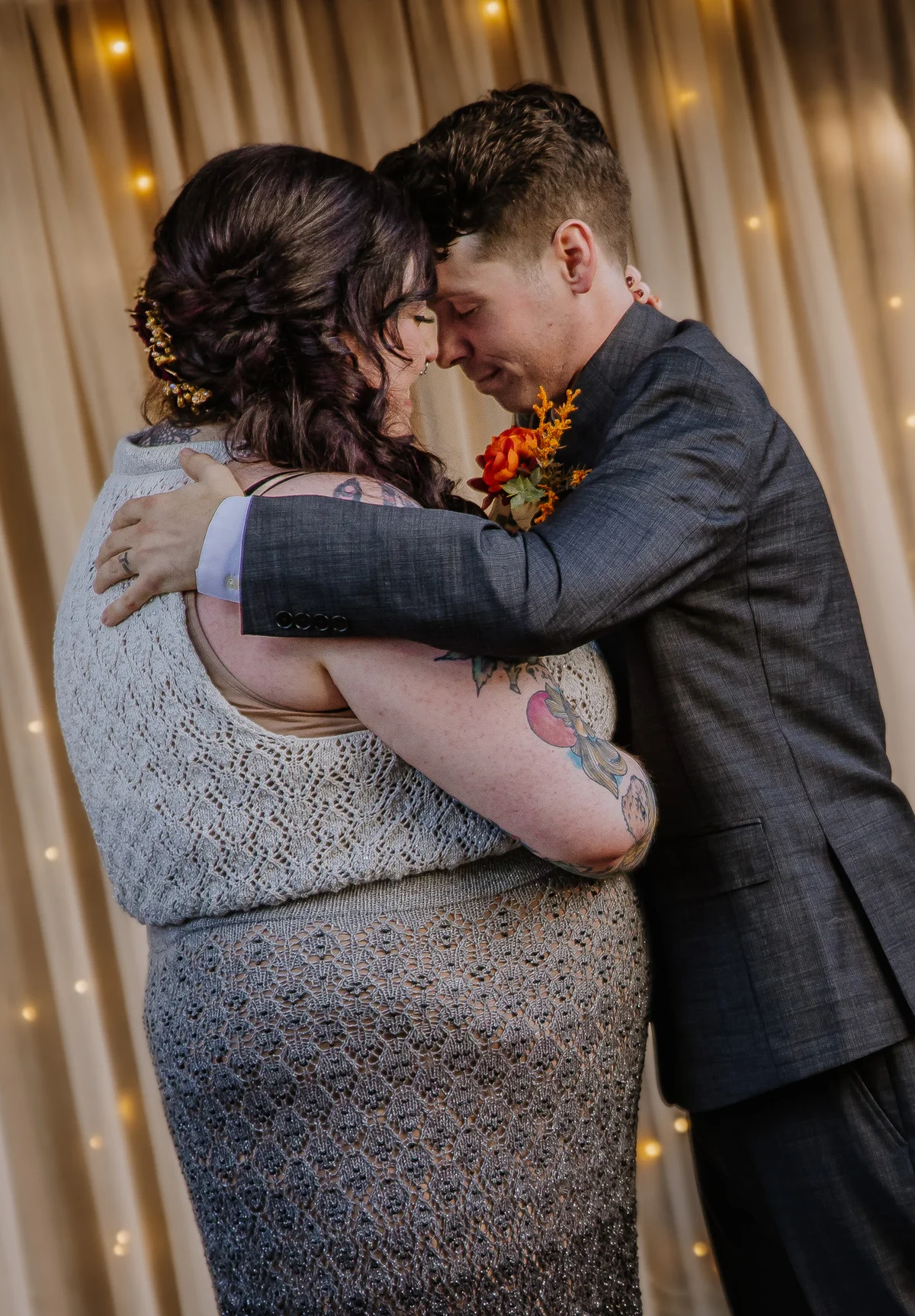 Bride and groom in a quiet embrace, foreheads resting together against a curtain of fairy lights