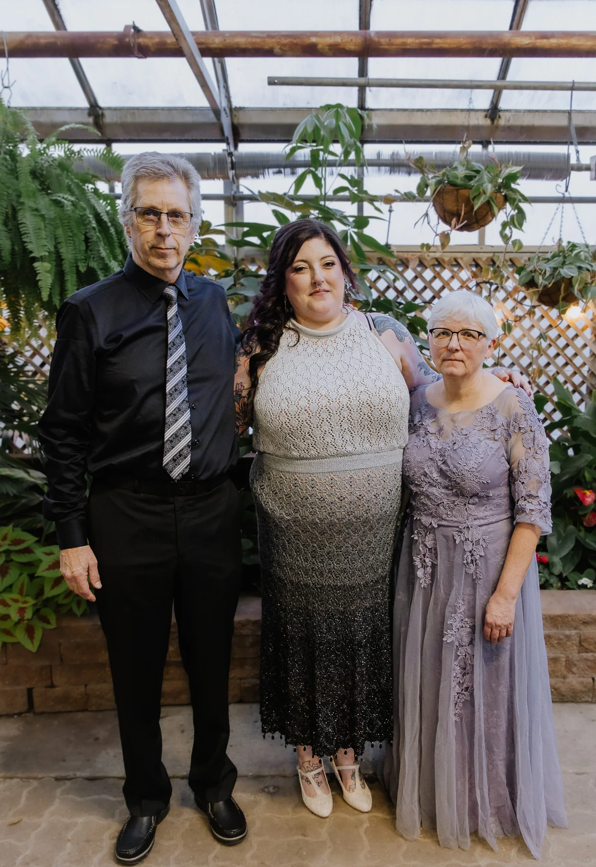 Bride with her parents on either side, formal family portrait in a greenhouse setting