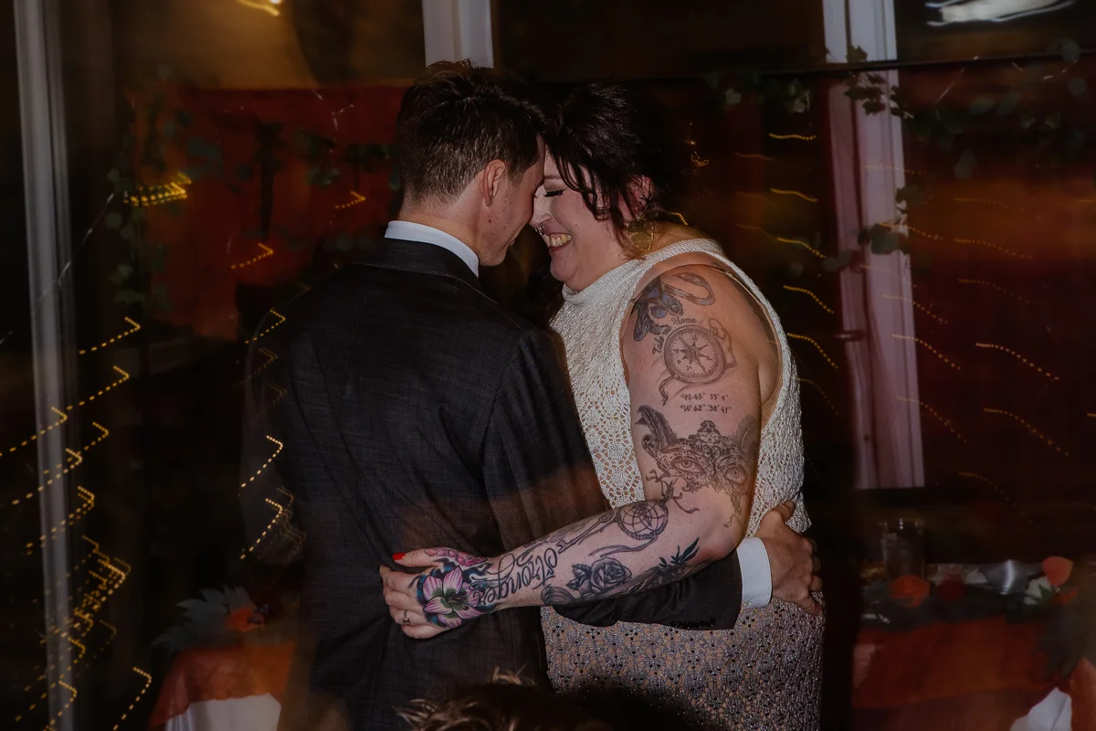 Newlyweds mid-first-dance, foreheads together, bride laughing in a beaded gown