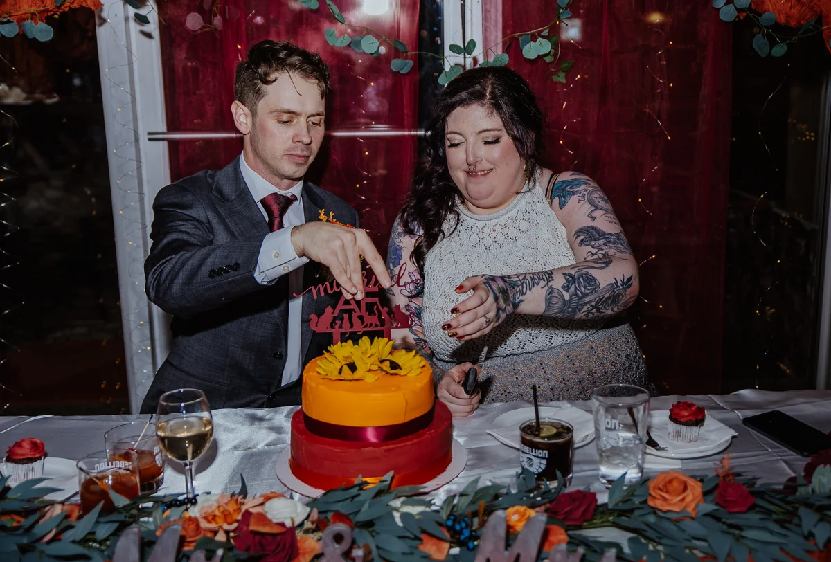 Bride and groom cutting a two-tier red and orange cake beneath a 'married AF' topper
